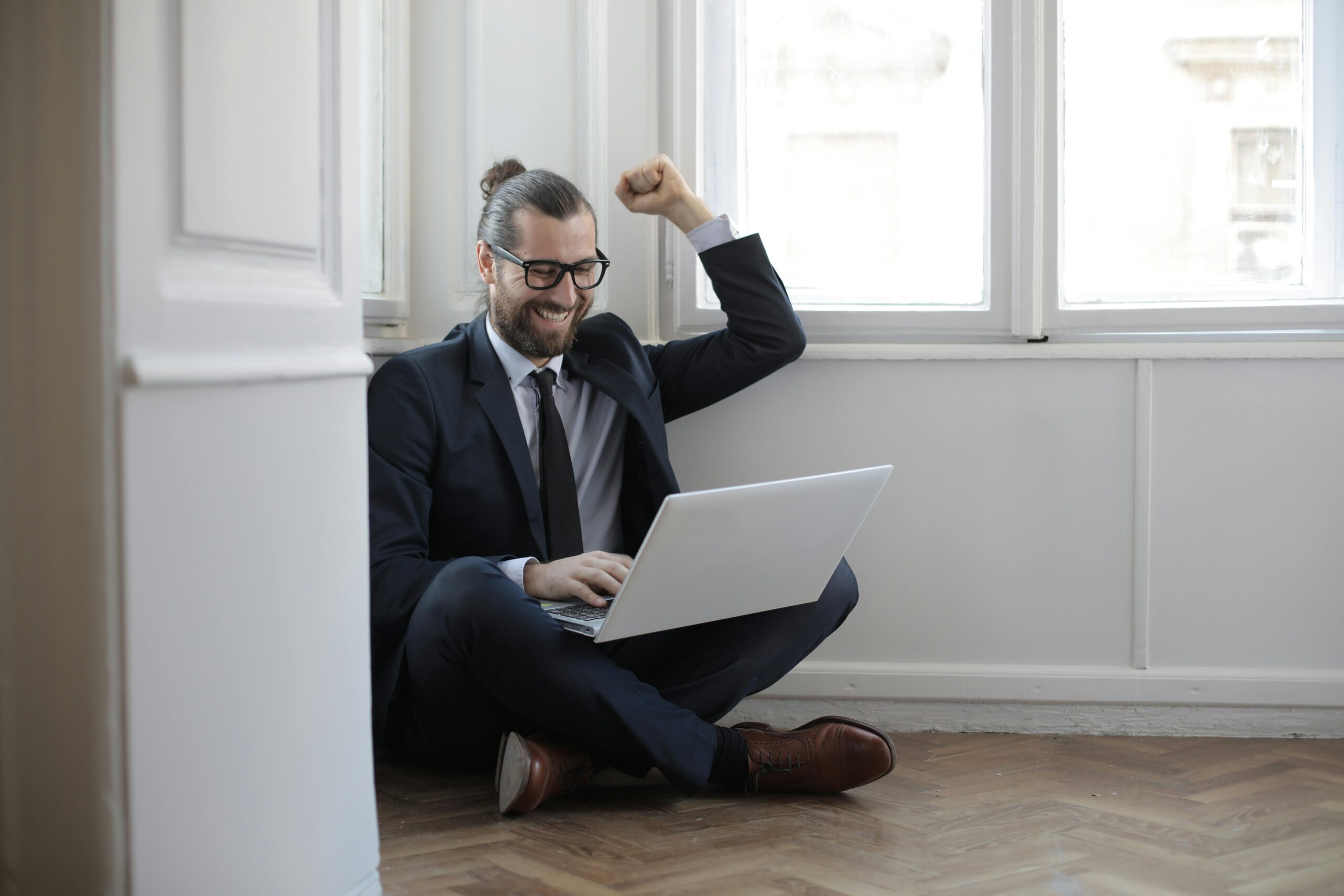 Cheerful man sitting on the floor with a laptop, celebrating work success.