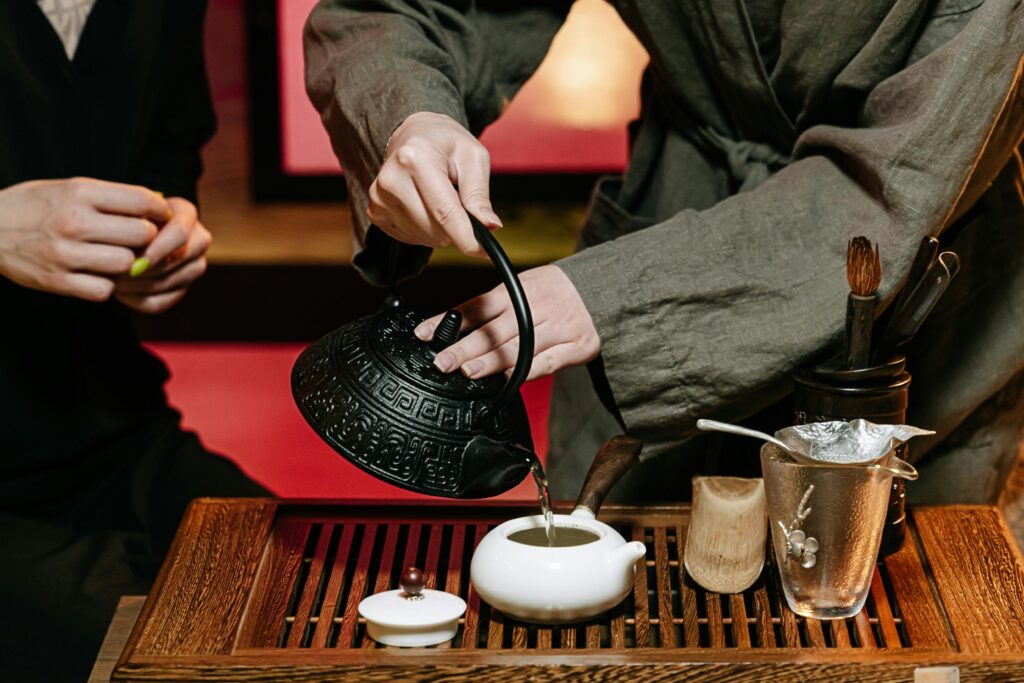 Close-up of a traditional tea ceremony showcasing hands pouring tea into a ceramic teapot on a wooden table.